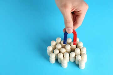 Man with magnet attracting wooden human figures on light blue background, closeup. Space for text