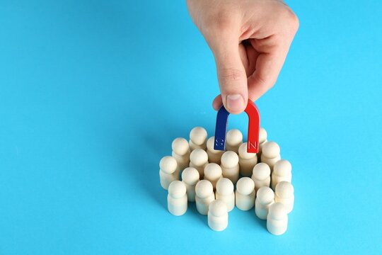 Man with magnet attracting wooden human figures on light blue background, closeup. Space for text