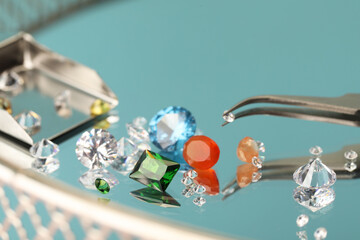 Beautiful colorful gemstones and tweezers on mirror surface, closeup