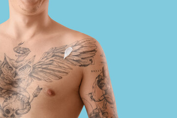 Tattooed young man with cream on blue background, closeup