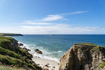La mer d'Iroise vue depuis les falaises du nord Finistère, ses eaux turquoises se mêlant au sable et aux rochers immergés. Le ciel bleu ajoute à l'harmonie de cette scène côtière.
