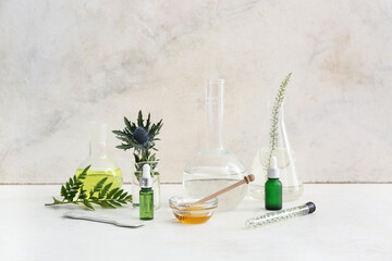 Bottles of oil, laboratory glassware with samples and ingredients for preparing natural cosmetics on white table near grunge wall