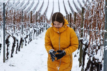Young woman in a mustard yellow winter coat hakes snow off her gloves after playing snowballs in a...