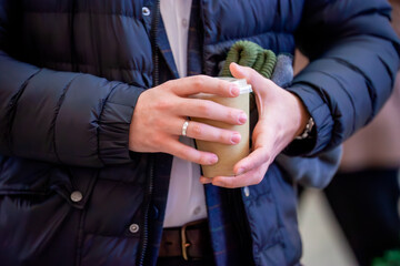 Close-up of a person holding a takeaway coffee cup, dressed warmly in a cozy jacket during a chilly...