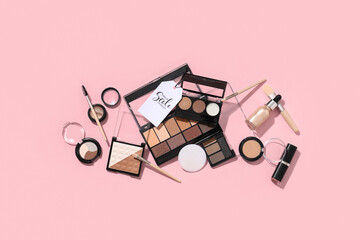 Composition with decorative cosmetics, makeup brushes and sale tag on pink background