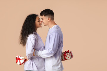 Loving young couple exchanging gift boxes on beige background. Valentine's Day celebration
