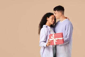 Loving young couple with gift box hugging on beige background. Valentine's Day celebration