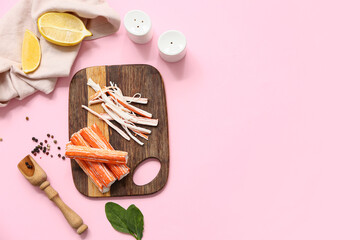 Wooden board with tasty crab sticks, cut lemon, spinach leaves and peppercorns on pink background © Pixel-Shot