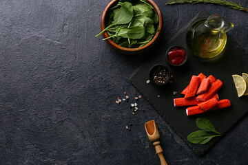 Black board with tasty crab sticks and different spices on dark background © Pixel-Shot
