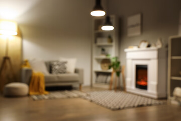 Blurred view of living room with fireplace, sofa and glowing lamps in evening