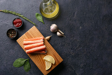 Wooden board with tasty crab sticks and different spices on dark background © Pixel-Shot