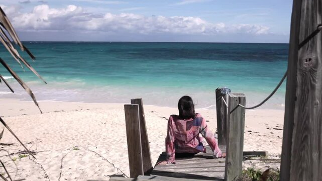 A woman sits on a dock overlooking the beach and the ocean in Elbow Cay in the Bahamas.