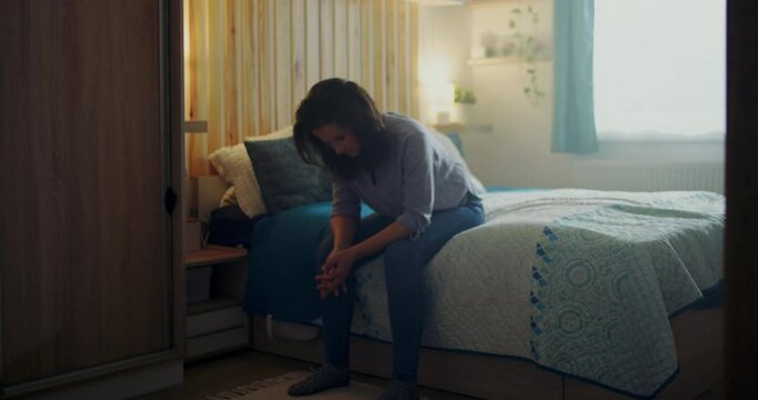 Woman sitting on a bed, leaning forward with her face buried in her hand, expressing raw emotions of despair, heartbreak, and deep personal sorrow
