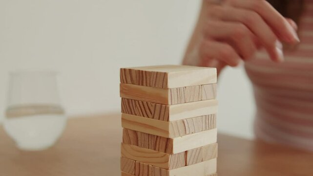 Woman carefully placing wooden block on top of tower. Focus, strategy, risk, and balance game.