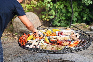 Grilling season. A man barbecues food outdoors in the spring. Delicious food cooked over a fire