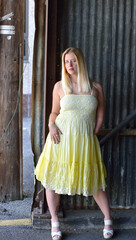 Attractive blonde woman in yellow dress poses for photo along a city alley