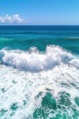 Fototapeta premium A stunning aerial view of turquoise ocean waves crashing against the shore under a bright blue sky.