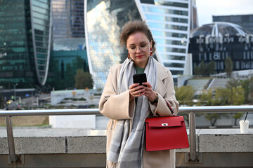 A young woman of European appearance writes a message in a messenger on a smartphone against the backdrop of Moscow City skyscrapers