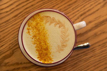 Table top view of porcelain cup of pumpkin latte made from espresso, milk, ground pumpkin seeds and ground nutmeg. Soft focus. Copy space. Interesting autumn season coffee drink theme.