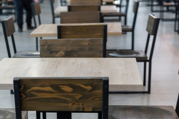 Close-up view of empty wooden tables of food court in shopping mall. Focus on table surface. Copy space for your text or decoration. Restaurant and cafe furniture. Food business theme.