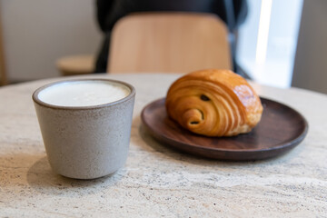 Close-up view of ceramic cup of white blank pumpkin latte made from espresso, milk and pumpkin puree with thyme standing by fresh croissant on table in coffeehouse. Soft focus. Copy space. Hot drinks.