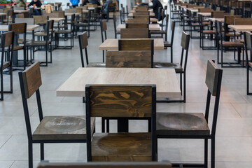 Close-up view of empty wooden tables of food court in shopping mall. Focus on table surface. Copy space for your text or decoration. Restaurant and cafe furniture. Food business theme.