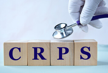 CRPS - acronym on wooden cubes with a doctor's hand with a stethoscope in the background