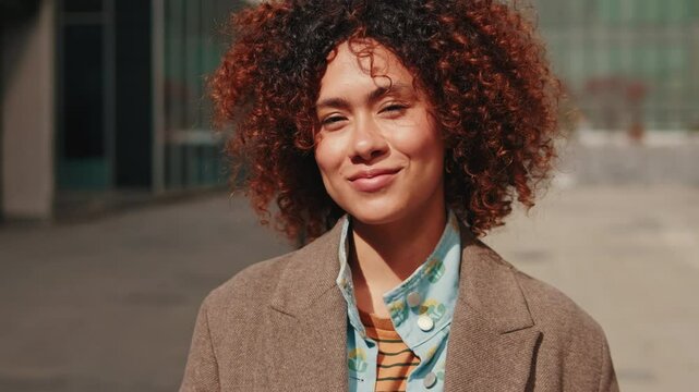 A stylish, happy, young woman walks towards the camera on a sunny day. Slow motion, medium shot.