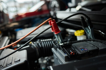 Closeup photo of black car battery connected with jumper cables for repair or recharging