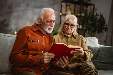 senior couple husband and wife sit on sofa and read a book together