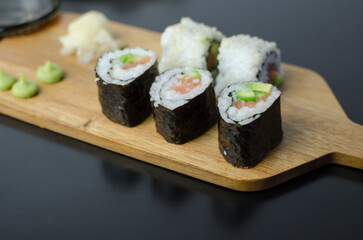 Homemade sushi rolls with salmon and avocado on a wooden board and grey plate, sushi selection, on a black backgroun