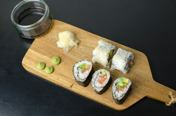 Homemade sushi rolls with salmon and avocado on a wooden board and grey plate, sushi selection, on a black backgroun