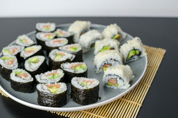 Homemade sushi rolls with salmon and avocado on a wooden board and grey plate, sushi selection, soy sauce, on a black background, top view