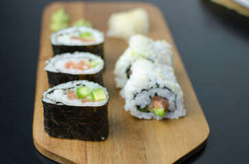Homemade sushi rolls with salmon and avocado on a wooden board and grey plate, sushi selection, on a black backgroun