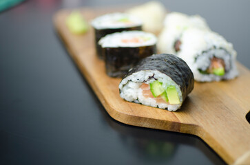 Homemade sushi rolls with salmon and avocado on a wooden board and grey plate, sushi selection, on a black backgroun