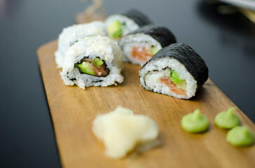 Homemade sushi rolls with salmon and avocado on a wooden board and grey plate, sushi selection, on a black backgroun