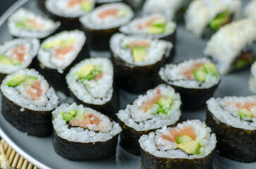 Homemade sushi rolls with salmon and avocado on a wooden board and grey plate, sushi selection, soy sauce, on a black background, top view