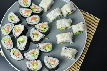 Homemade sushi rolls with salmon and avocado on a wooden board and grey plate, sushi selection, soy sauce, on a black background, top view
