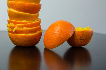 Orange halves, orange peel on a black table, white wall, shadows, lights