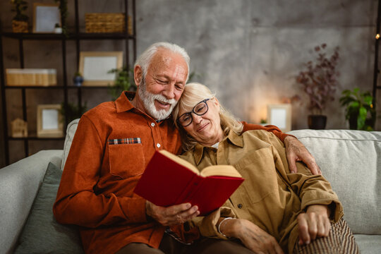 senior couple husband and wife sit on sofa and read a book together