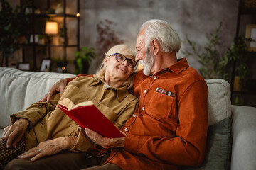 senior couple husband and wife sit on sofa and read a book together