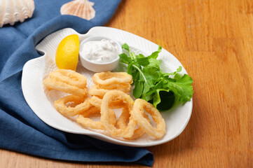 A beautiful presentation of fried calamari, squid with white sauce, lemon and arugula leaves on the side