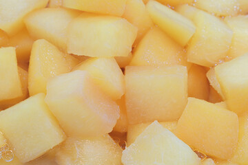 A close up of a pile of yellow fruit cubes. The fruit cubes are frozen and appear to be cut into small pieces. Concept of abundance and freshness, as the fruit cubes are piled high