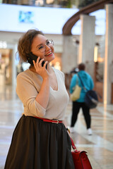 Fototapeta premium A young woman of European appearance is talking on the phone in a shopping mall