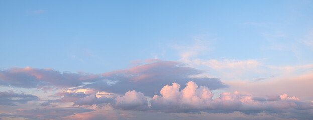 A blue sky panorama with a few clouds. The clouds are white and pink. The sky is clear and bright