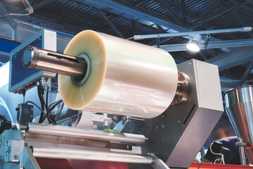 A roll of plastic film above a packaging conveyor for food packaging or plastic packaging bag...