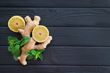 Ginger, Lemon, and Mint on Black Wooden Background. Fresh ginger root, lemon slices, and mint leaves arranged on a textured black wooden surface. Top view. Free space for text.