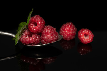 Close-up of fresh red raspberries on a metal spoon. The spoon lies in front of a dark background...