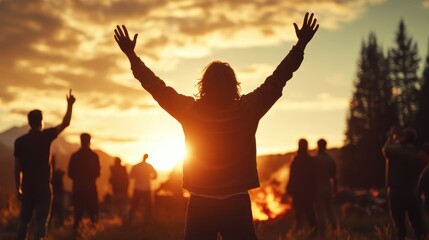 Fototapeta premium A group gathers in a scenic outdoor setting, raising arms in joy near a warm campfire under a striking sunset, evoking themes of celebration and togetherness.