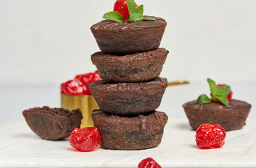 Chocolate brownies with the top adorned by a red juicy cherry and mint leaves, white background